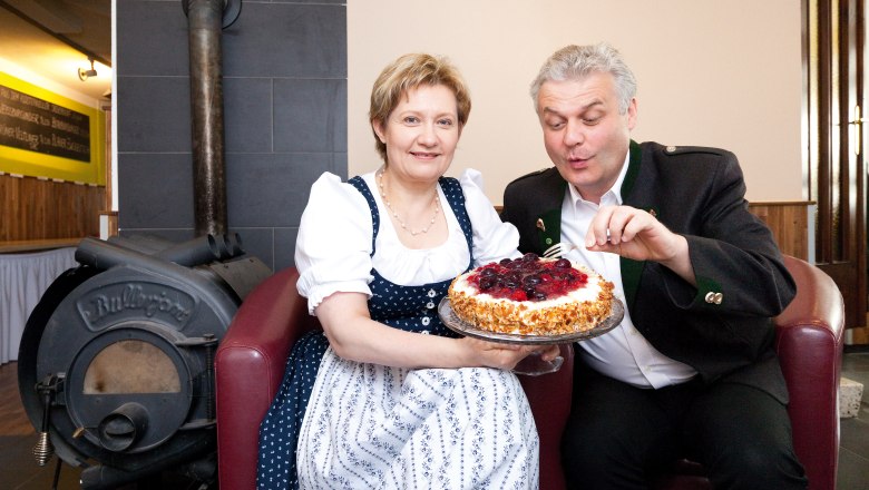 A man and a woman in traditional dress hold a cake in front of an oven.