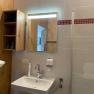 Modern bathroom with washbasin, mirror, wooden shelf and shower cubicle.