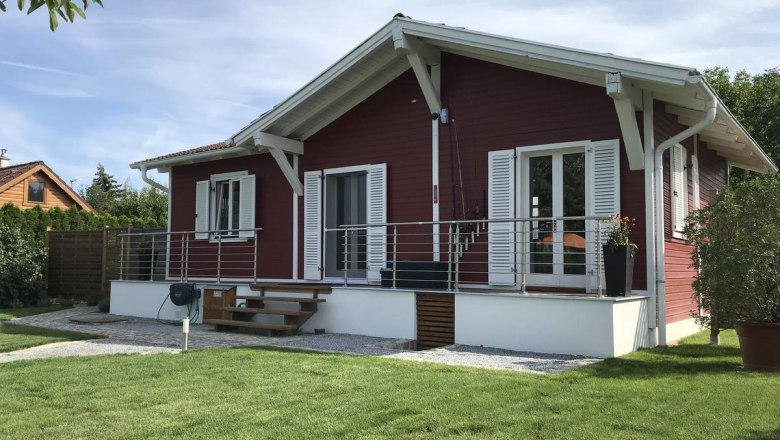 A red wooden house with a white roof and shutters, surrounded by a well-tended garden.