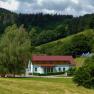 A vacation farm with red roofs in a green, hilly landscape with trees and meadows.