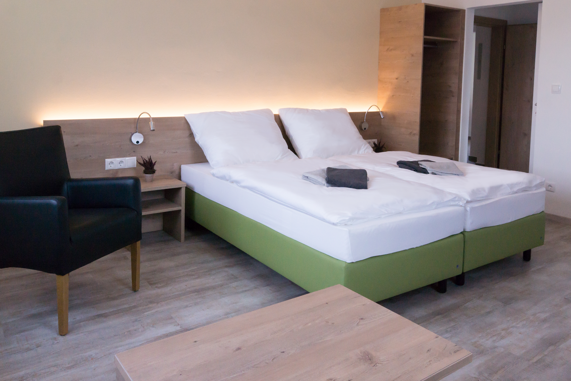 Modern furnished hotel room with double bed, bedside table, armchair and closet.
