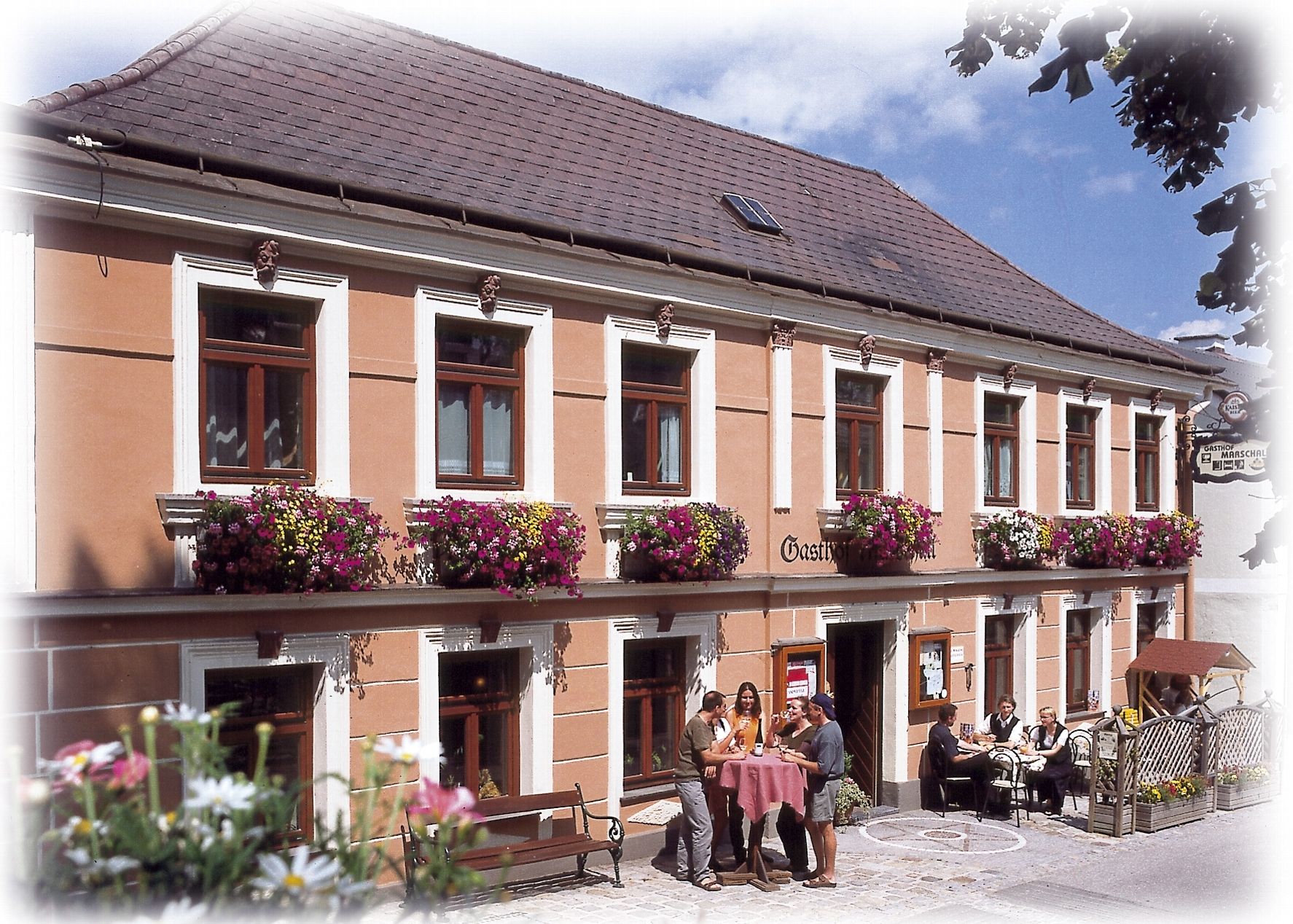 A traditional inn with a flower-decorated façade and guests sitting at tables outside.