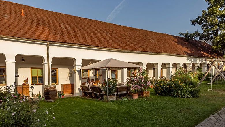 A traditional winery with white arcades, a red tiled roof and a garden with a seating area and flowers.