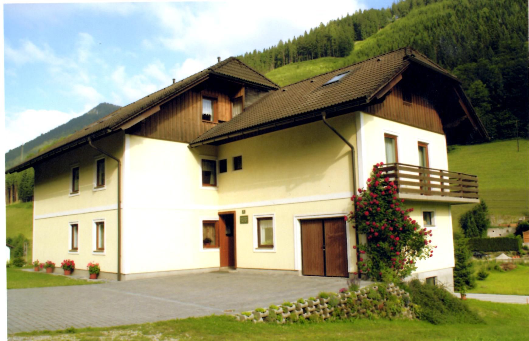 A two-storey house with a balcony and rose bush, surrounded by green hills.