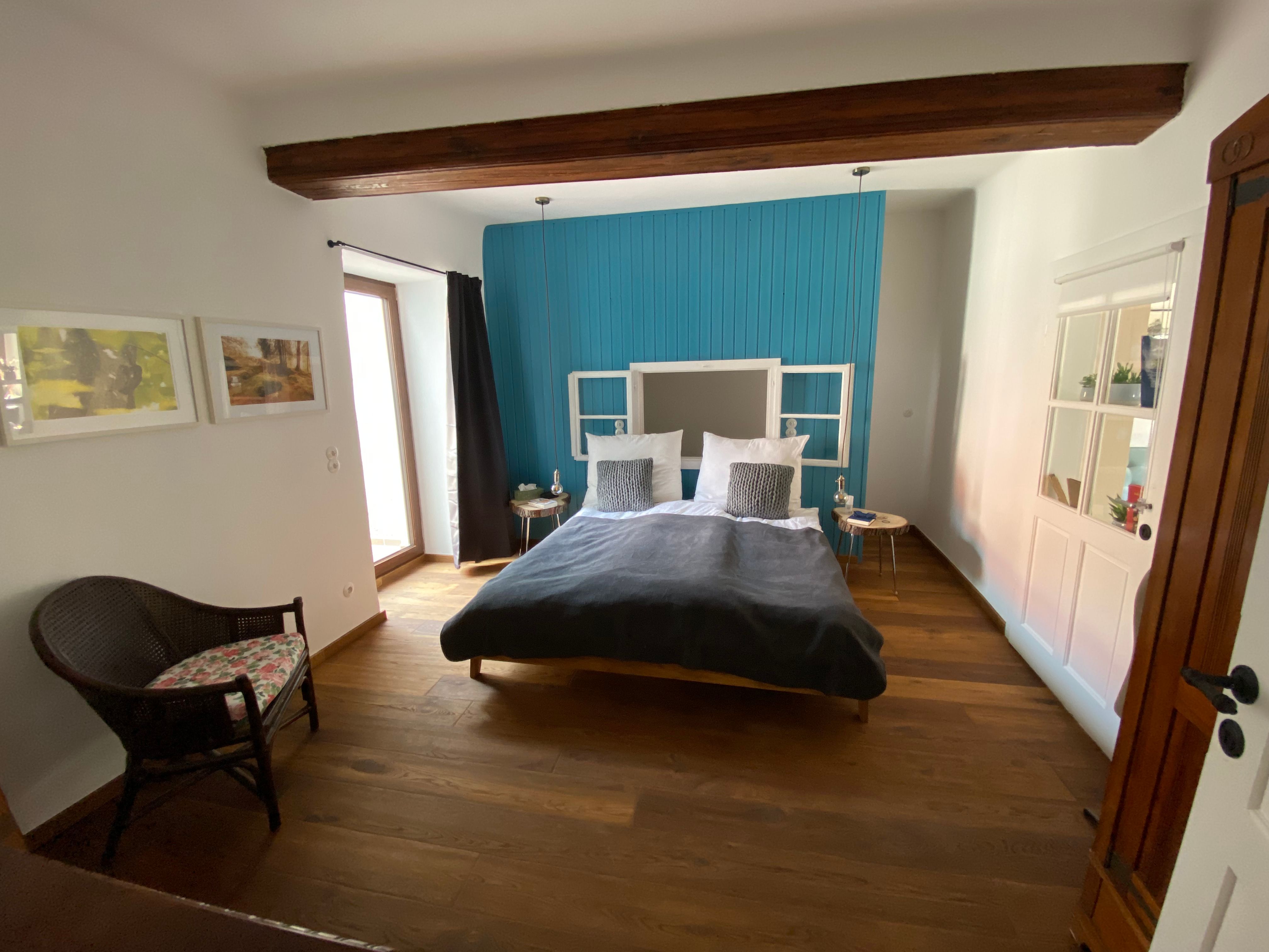 Modern bedroom with wooden floor, blue accent on the wall, double bed and rattan chair.
