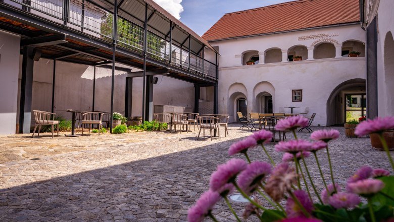 forty yard, © Niederösterreich Werbung / Maximilian Pawlikowsky An inner courtyard with cobblestones, tables and chairs, surrounded by buildings with arcades and a modern balcony.