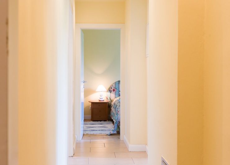 A bright hallway leads to a bedroom with bedside lamp.