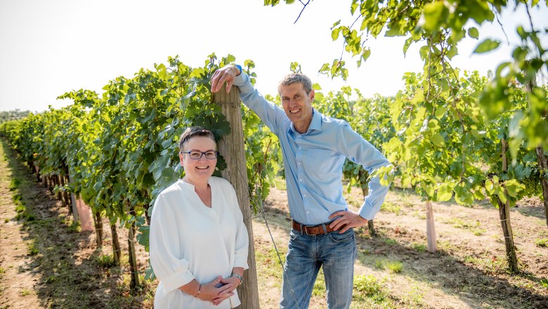 A man and a woman stand smiling in a vineyard.