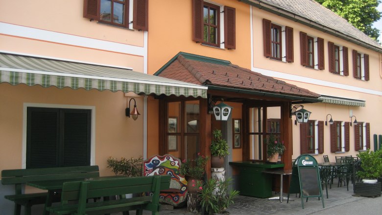 Entrance to a traditional inn with an orange façade and green wooden furniture outside.