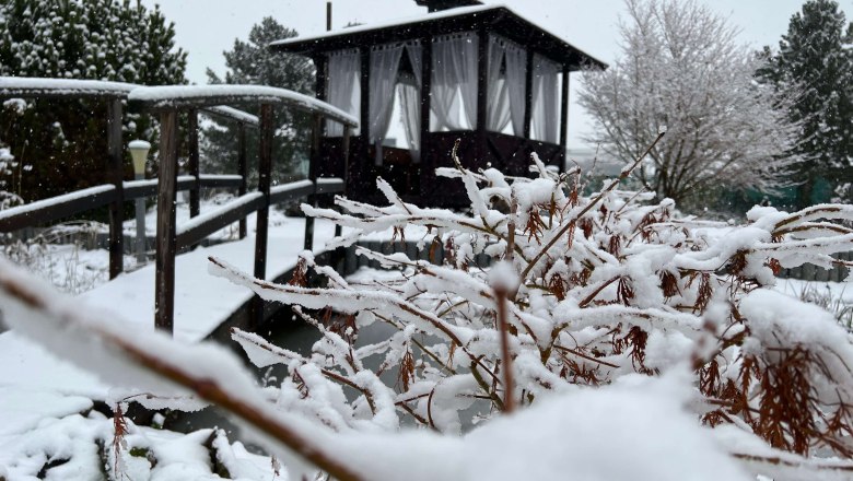 Snow-covered Zen garden with wooden bridge and pavilion in the background.