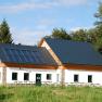 A hut with solar panels on the roof, surrounded by trees and meadows.