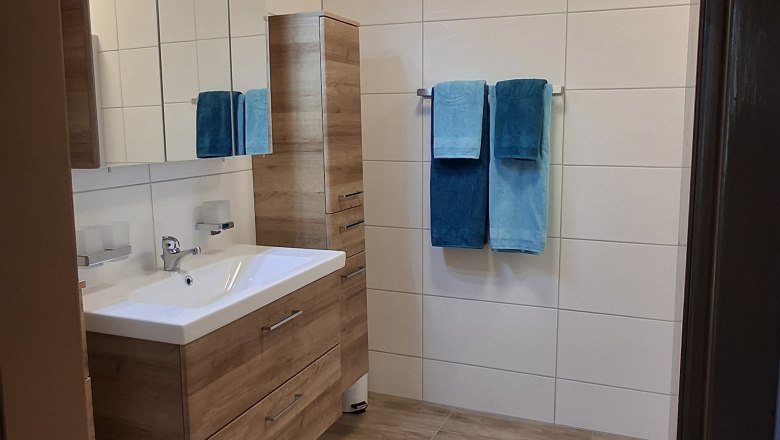 Modern bathroom with wooden ceiling, washbasin, mirror, towels and carpet.