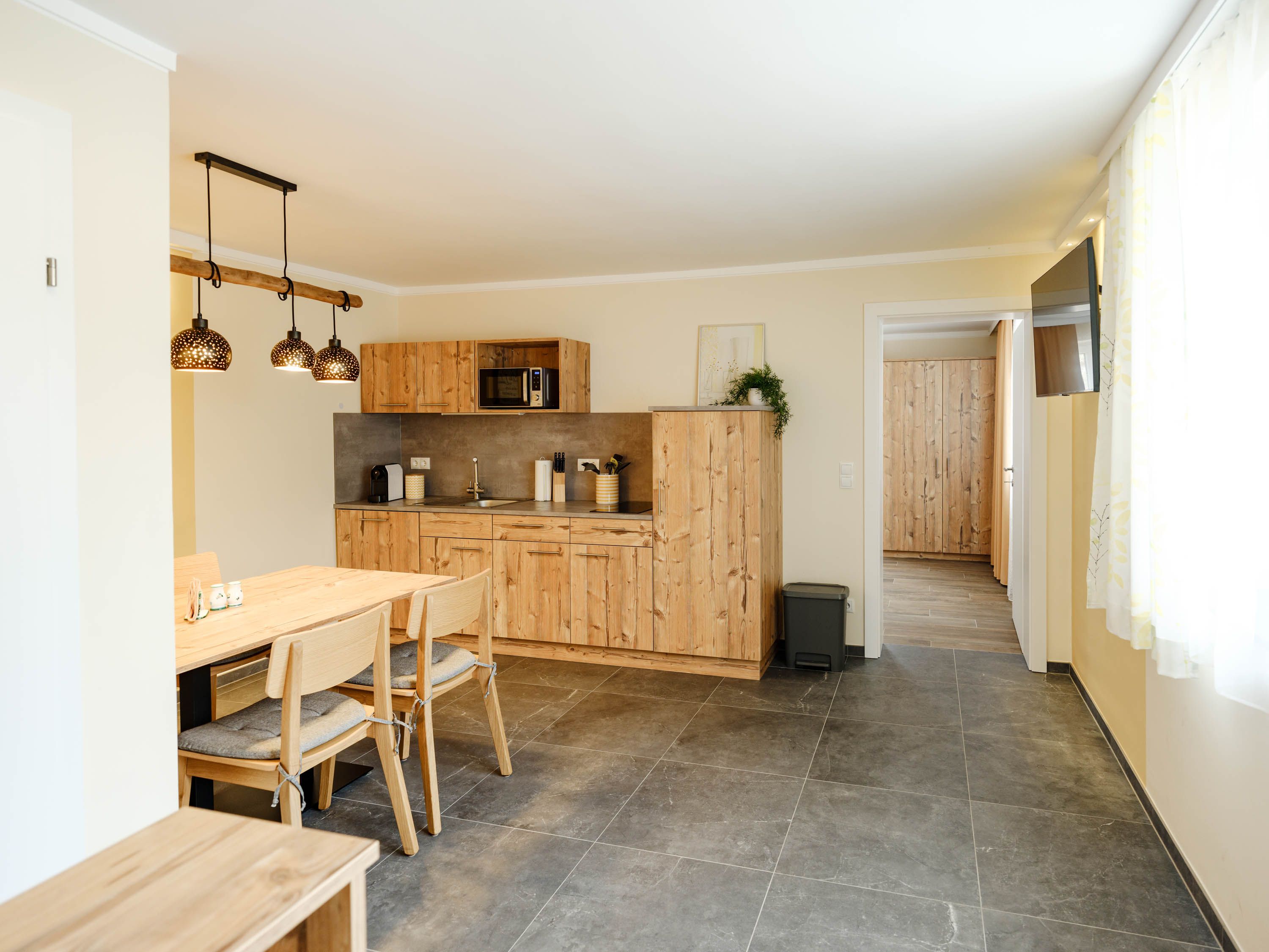 Modern kitchen with wooden furniture and dining table, bright lighting.