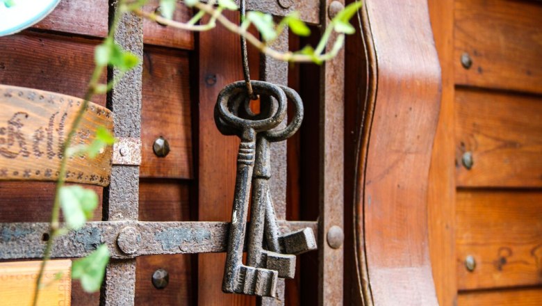 An old cellar key hangs on a rusty grille in front of a wooden wall.