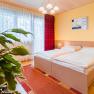 Cozy bedroom with double bed, yellow wall, red carpet and plants in the foreground.