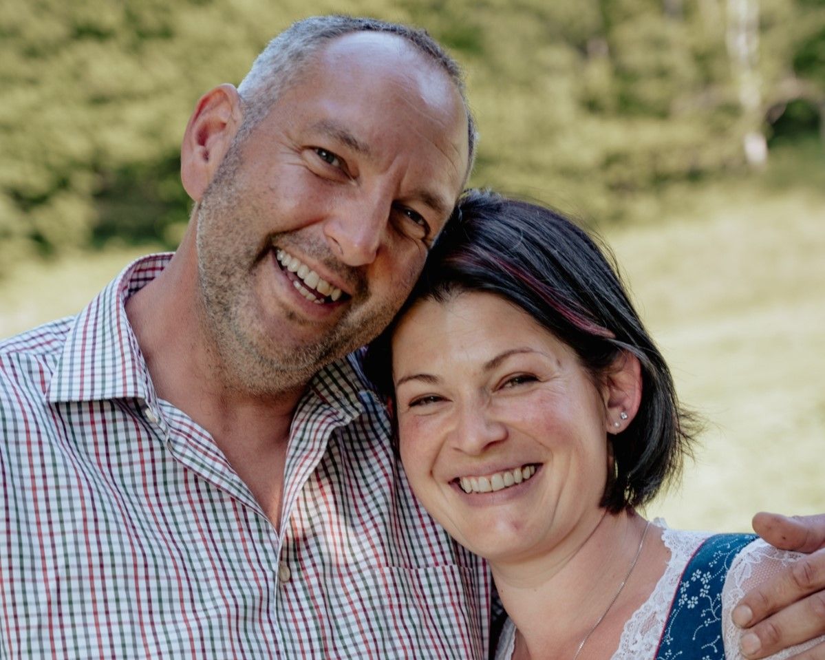 A smiling couple is posing outdoors on a meadow.