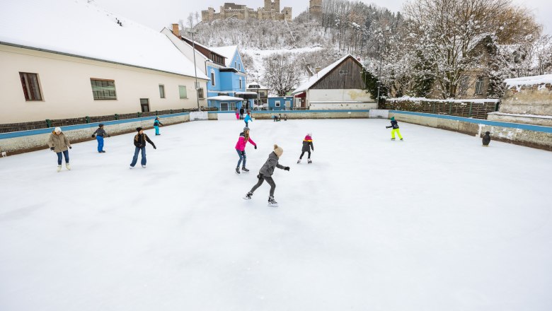 People skating on a square in Kirchschlag, with a castle ruin on a hill in the background.