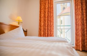 Double bed with white bed linen. In the background a floor-to-ceiling window with a view of the church.