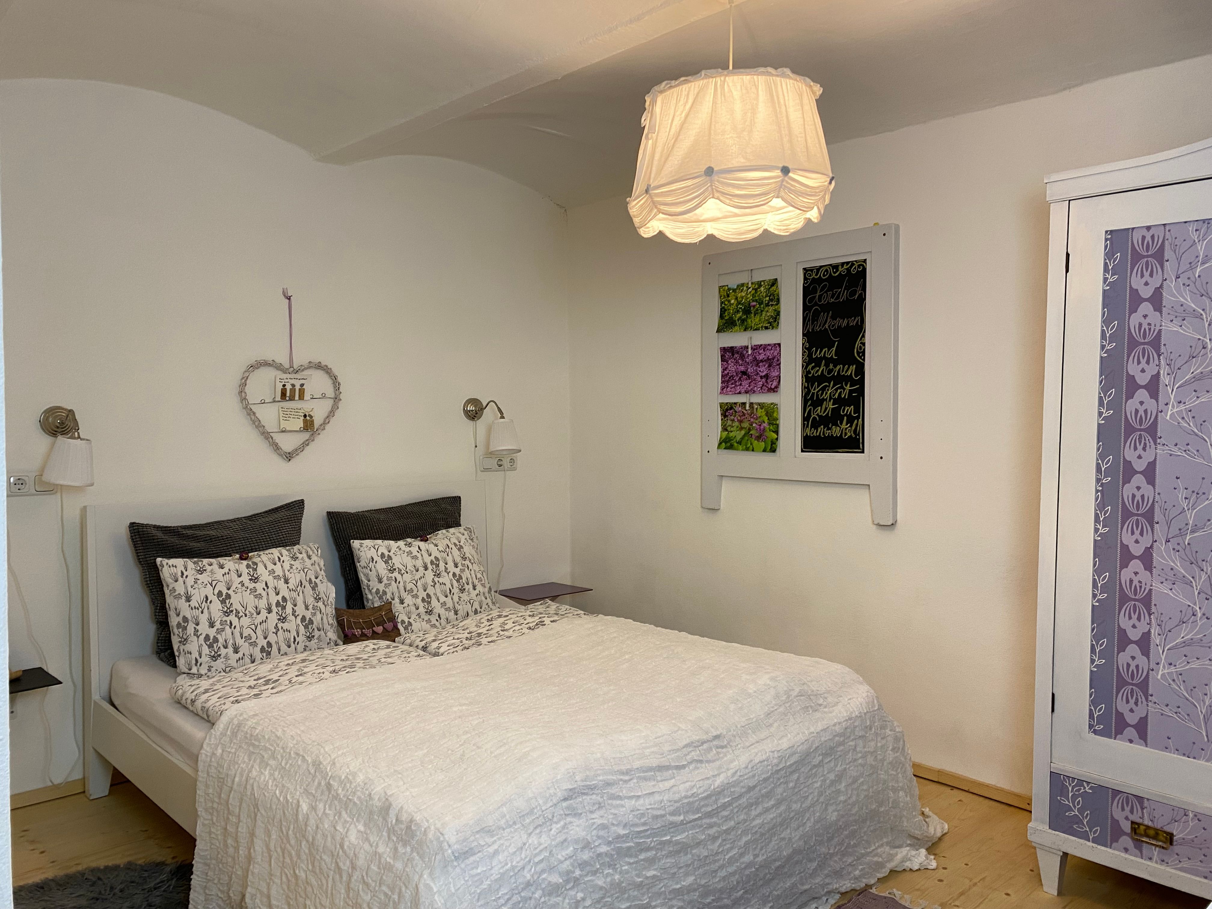 Cozy double room with white bed, decorative heart shelf and purple wardrobe.