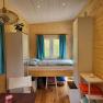 Small room with wooden walls, fold-down bed, blue curtains and shelves.