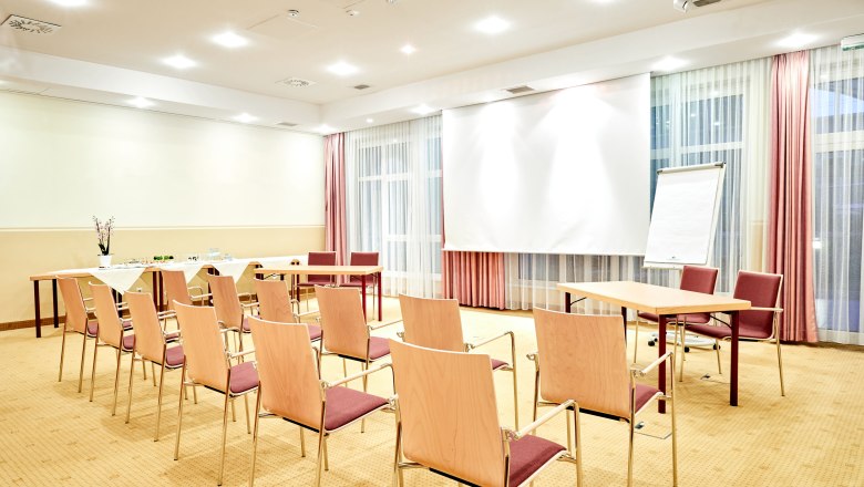 A bright seminar room with chairs, tables, a flipchart and a projection screen.