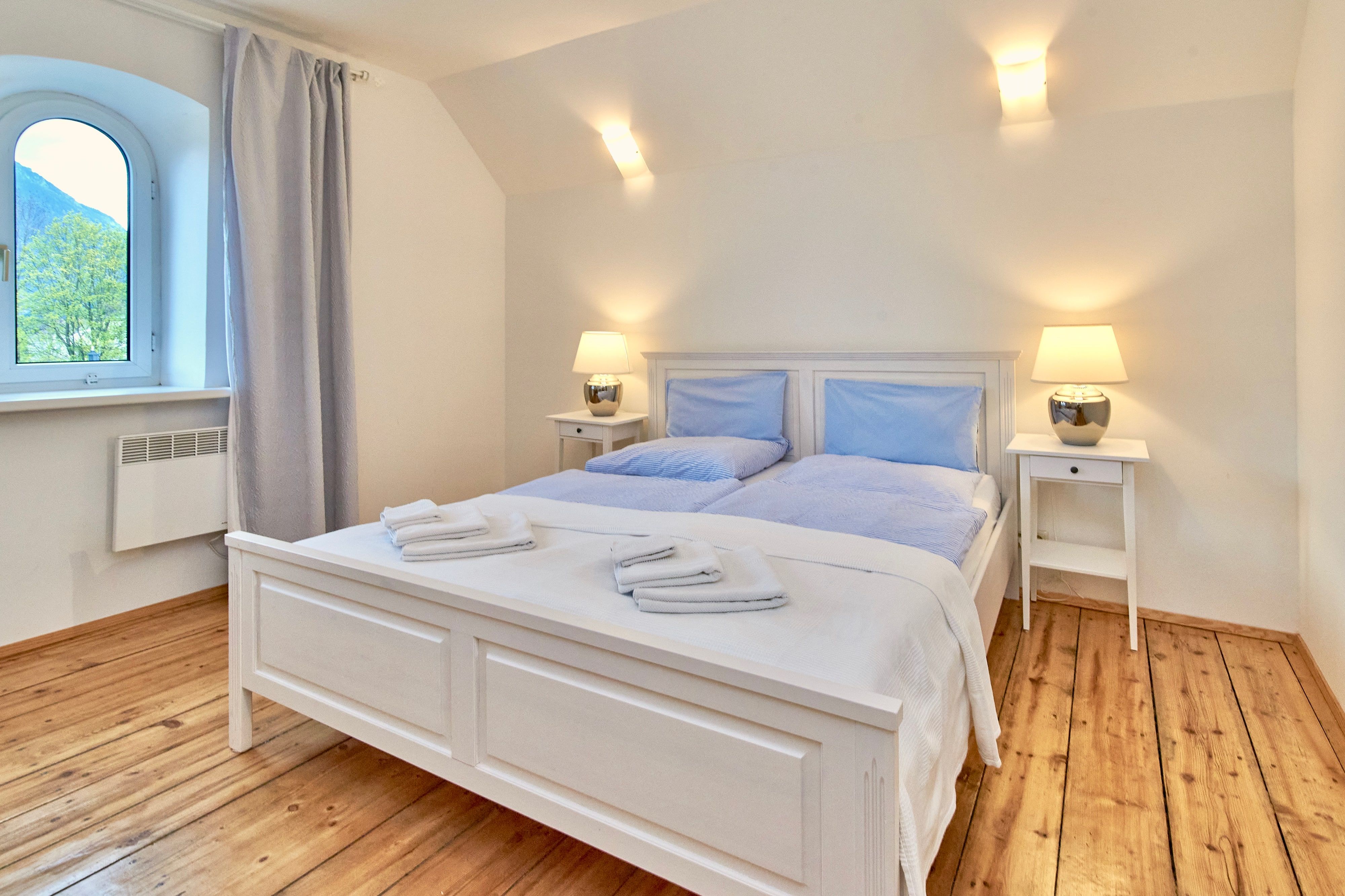 Bright bedroom with double bed, wooden floor and two bedside tables with lamps.