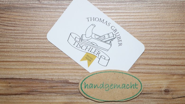 Business card of carpenter Thomas Gruber with a slicer logo and a handmade label on a wooden background.