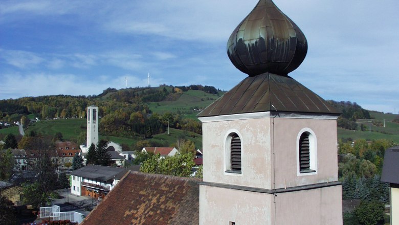 Church tower with onion roof in front of a hilly landscape and wind turbines.