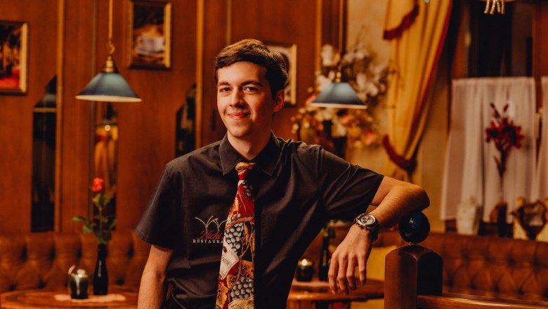 Young man in a restaurant with tie and shirt, smiling.