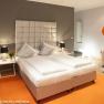 Modern hotel room with double bed, orange wall decoration and stylish armchair.