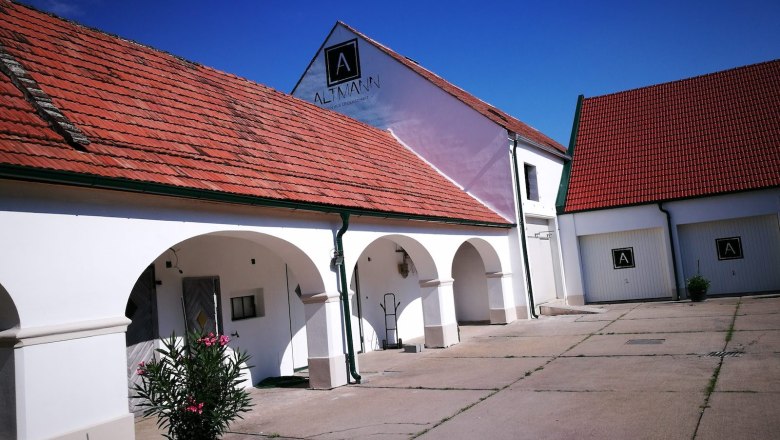 White building with red tiled roofs and arcades, blue sky.