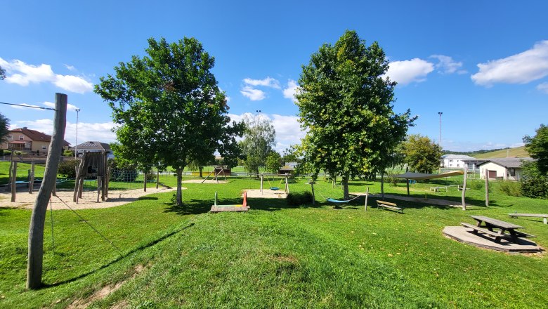 A playground with a climbing frame, swings and picnic table on a green meadow under a blue sky.