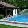 Two children swim in a small, covered pool next to a wooden pavilion.