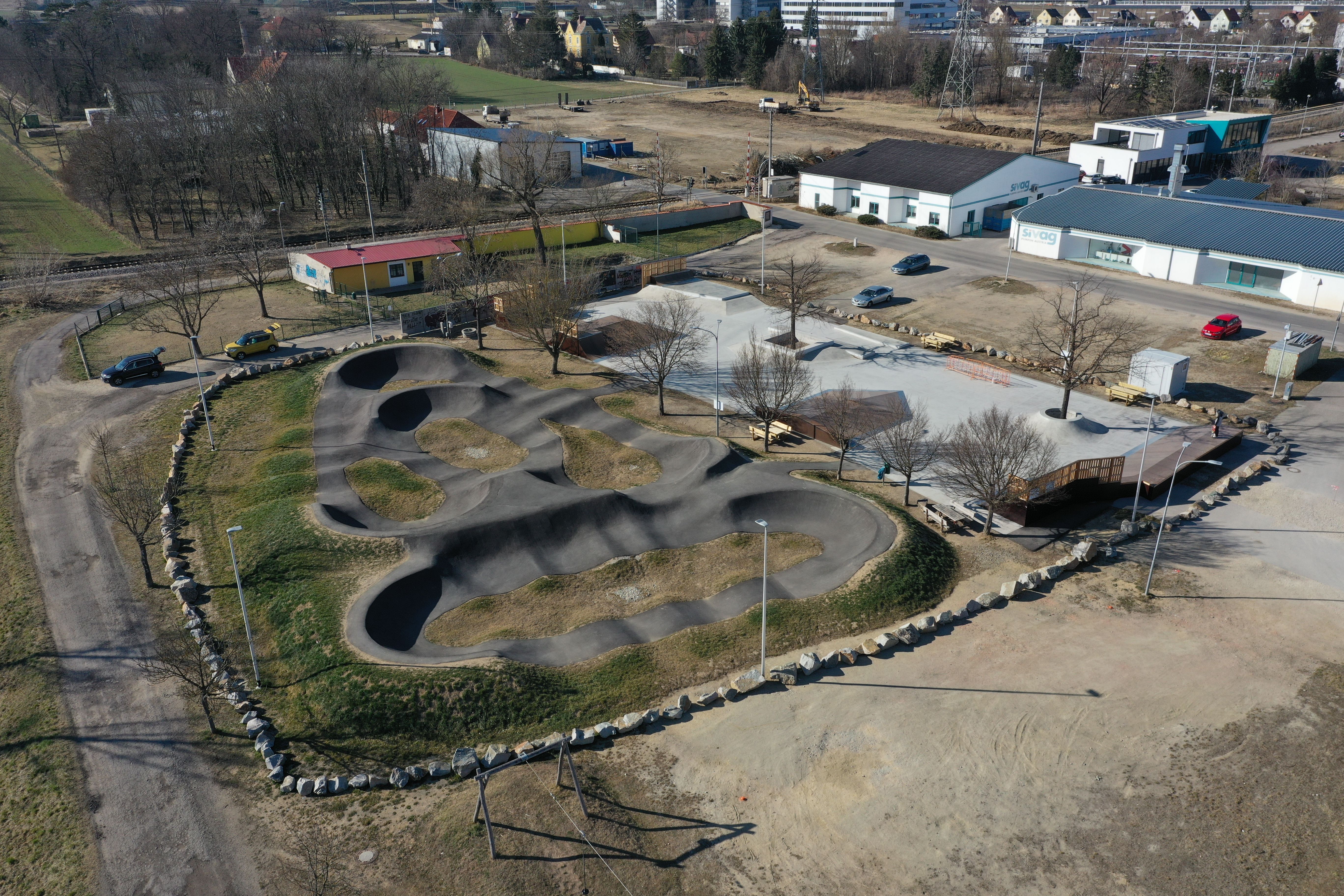 Aerial view of a pump track with surrounding buildings and parking lots.