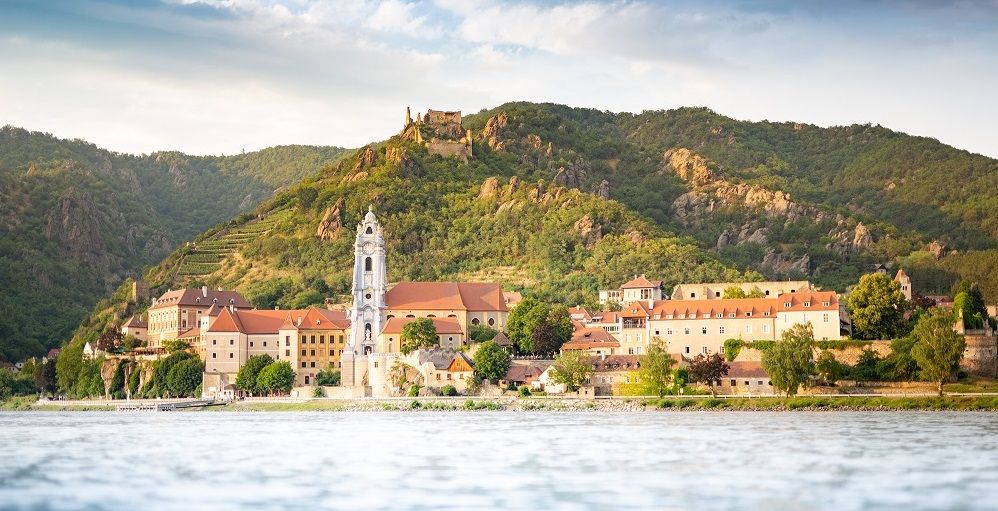 View of Dürnstein with monastery and castle ruins in front of wooded hills.