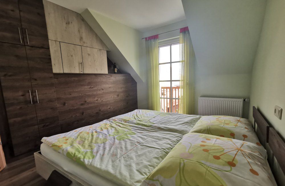 Bedroom with double bed, wooden wardrobe and window with yellow curtains.