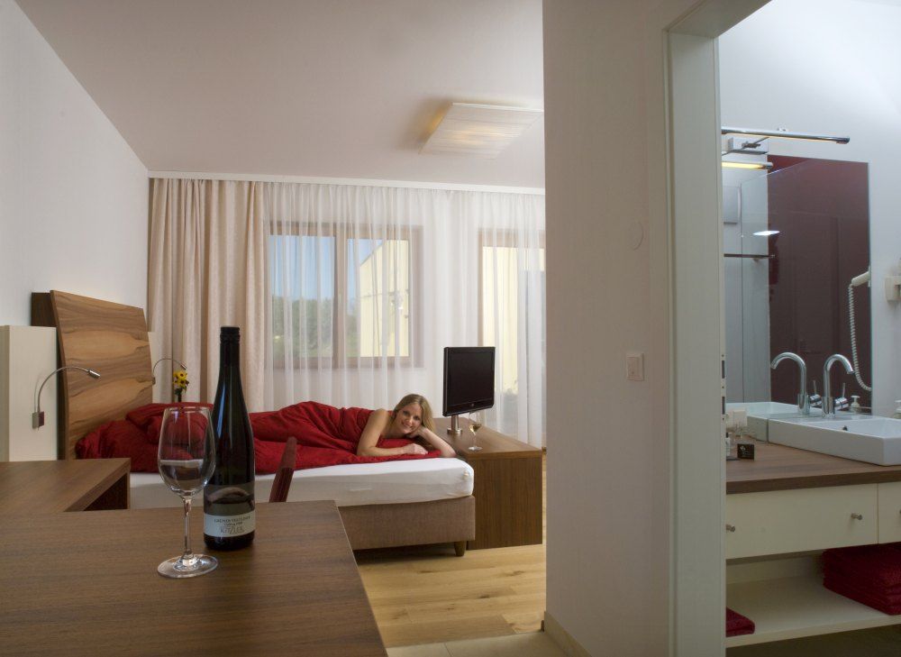 A modern hotel room with a bed on which one person lies and a table with a bottle of wine and a glass.