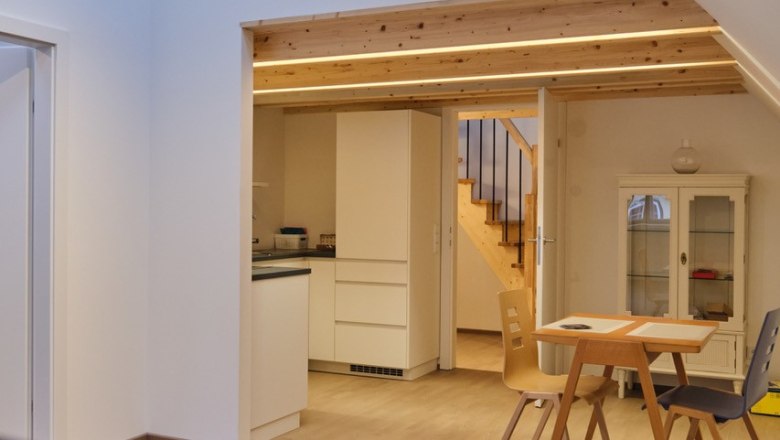 Interior view of a modern living room with wooden staircase, dining table and kitchen area.
