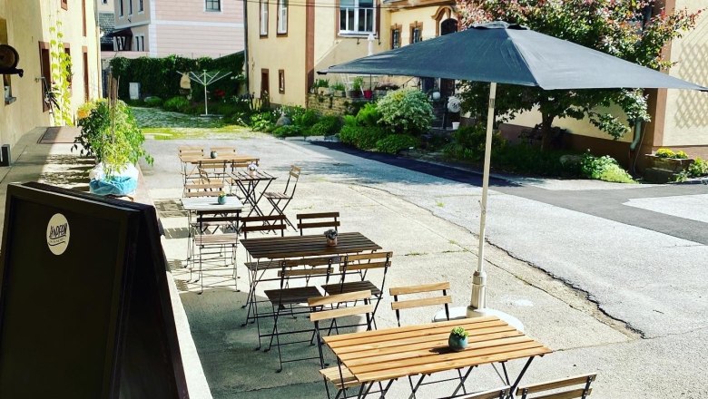 A guest garden with wooden tables and chairs, a parasol and plants in an inner courtyard.