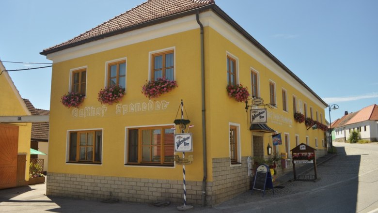 Yellow building with the inscription 'Gasthof Speneder', decorated with flowers.