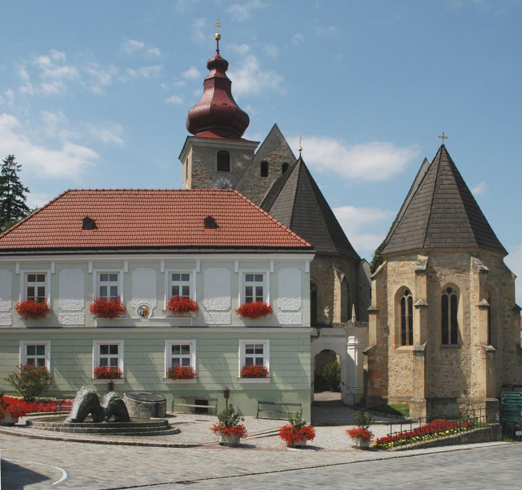 Historic building with red roof and church in the background on the Maria-Anzbach market square.