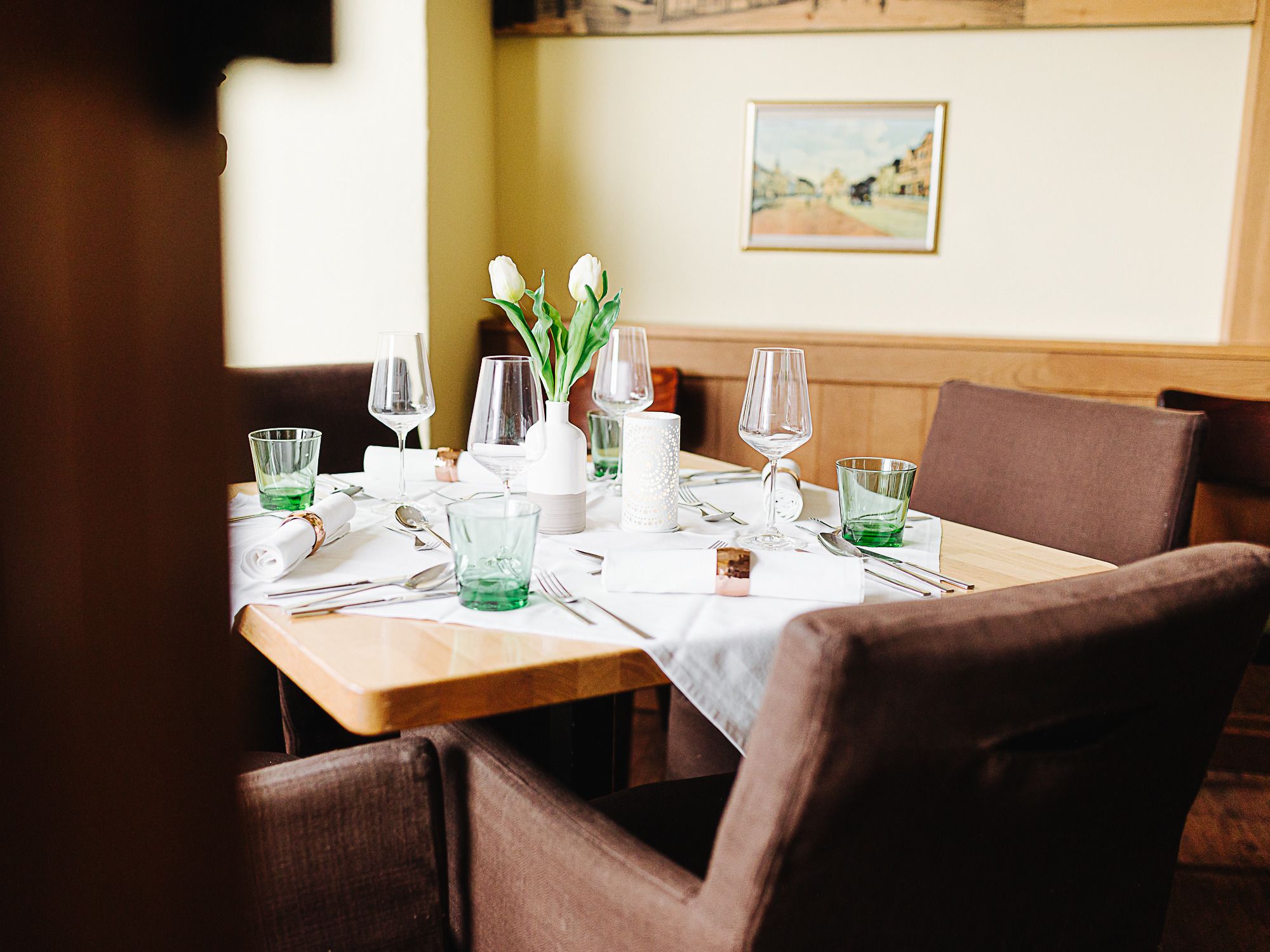 An elegantly laid table in an inn with glasses, cutlery and white tulips in a vase.