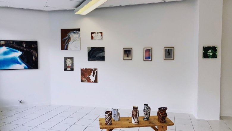Gallery room with works of art on the wall and ceramics on a wooden table.