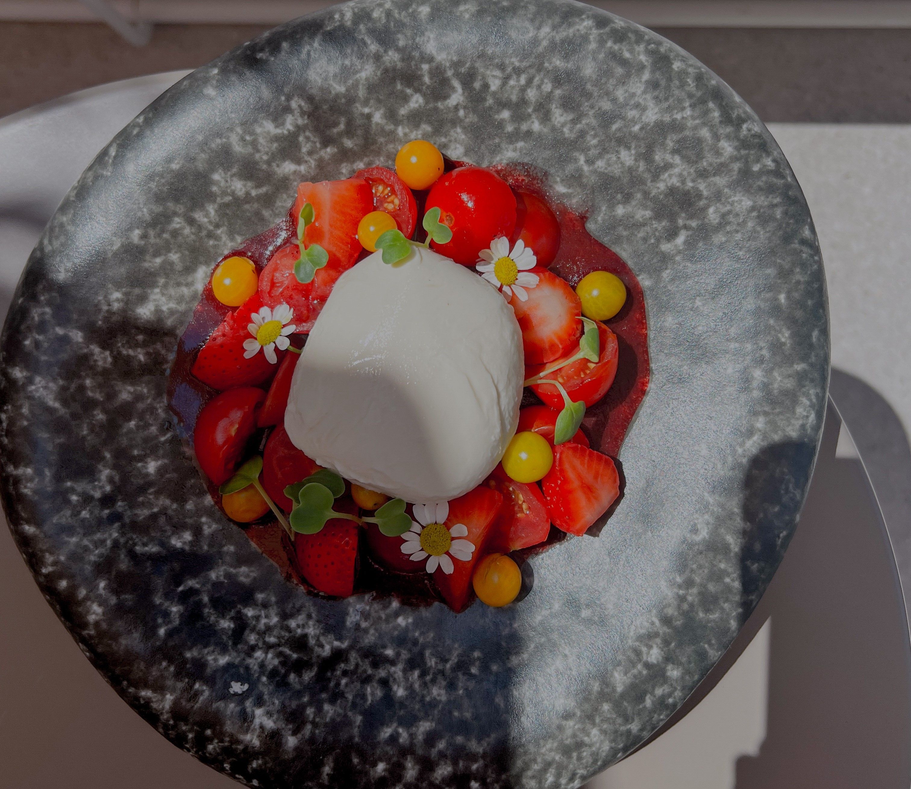 A plate of burrata, strawberries, tomatoes and edible flowers.