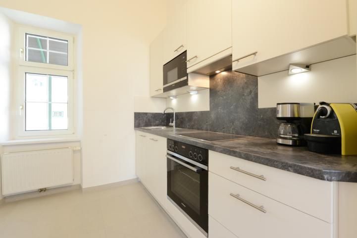 Modern kitchen with white cupboards, gray worktop, oven, microwave and coffee machines.