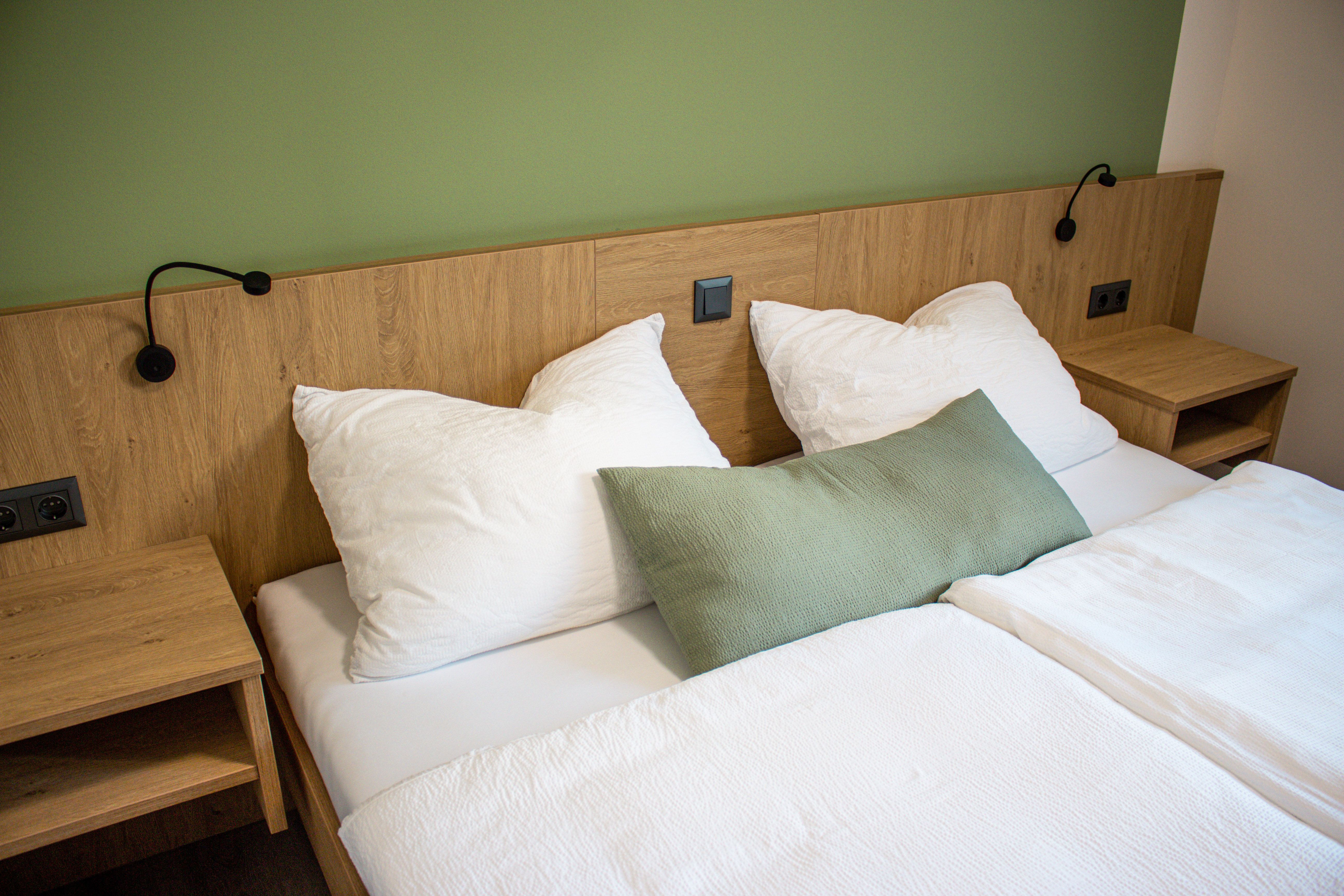 A double bed with white bed linen and a green wall in the background.