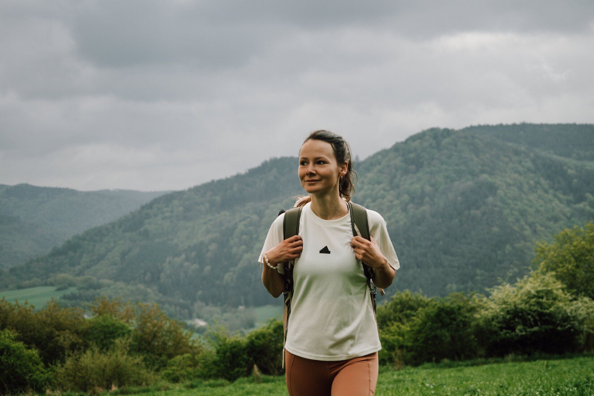 A hiker enjoys the fresh mountain air and the breathtaking view of the rolling hills and dense forests. The clouds in the sky lend the scenery a mystical atmosphere, while nature is in full bloom. This idyllic setting invites you to unwind and explore the beauty of the surroundings.