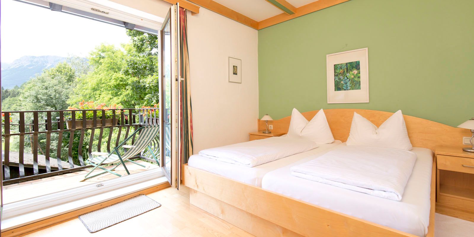 Bright room with double bed, green-painted wall and balcony with mountain view.