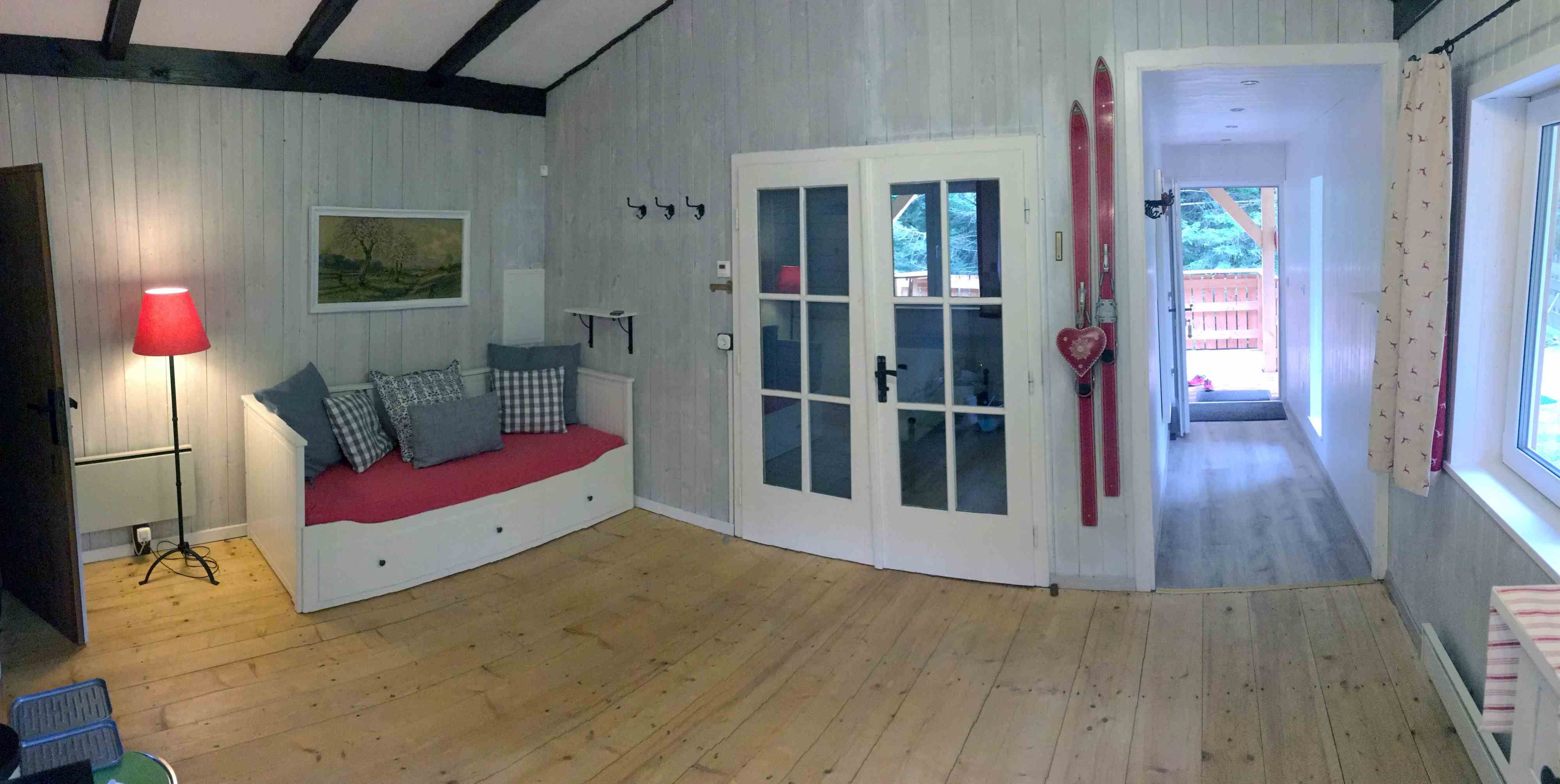 Interior view of a cozy vacation home with wooden floor, red sofa, skis on the wall and glass doors.