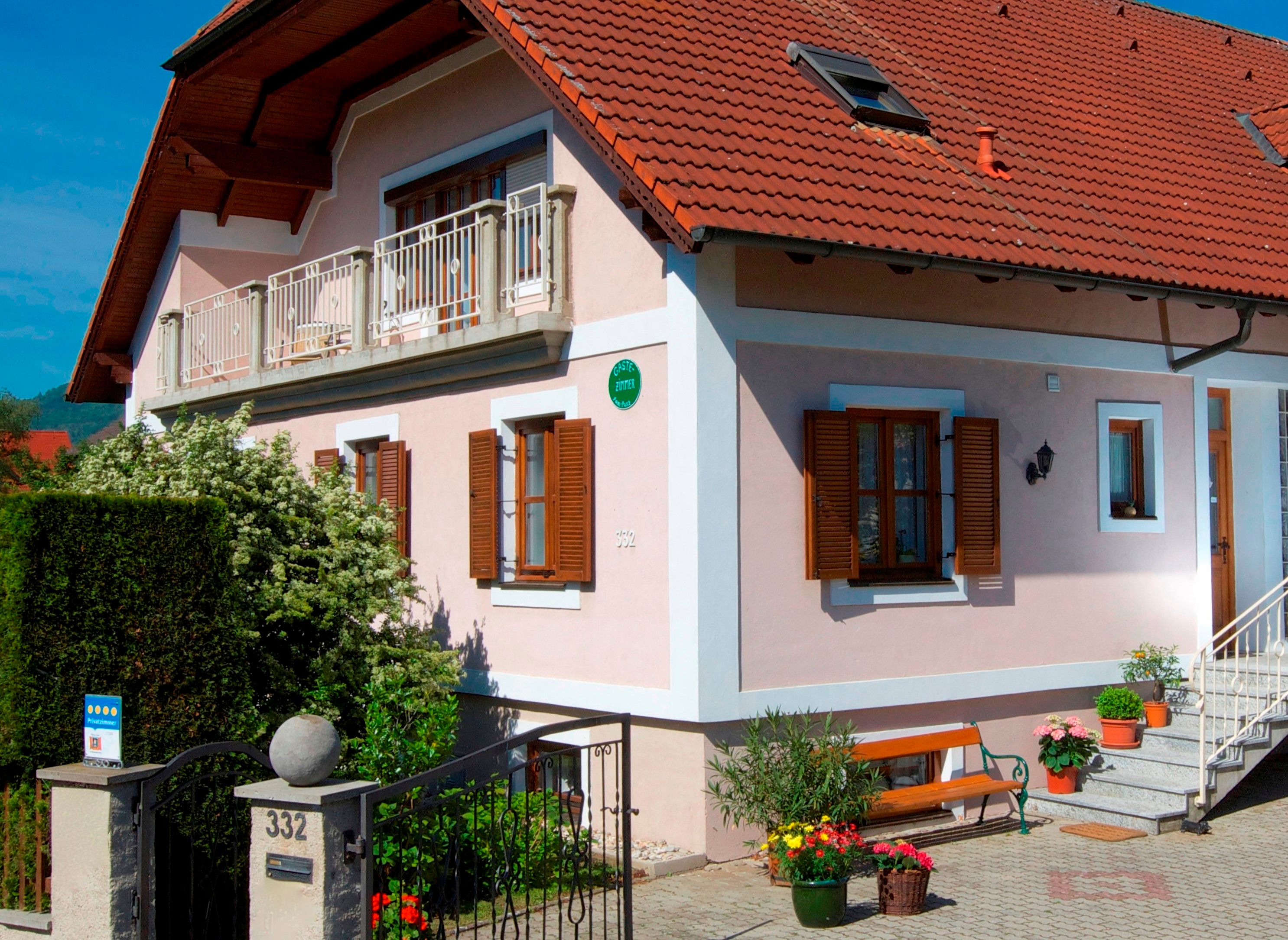 A two-storey house with a red tiled roof, balcony and garden.